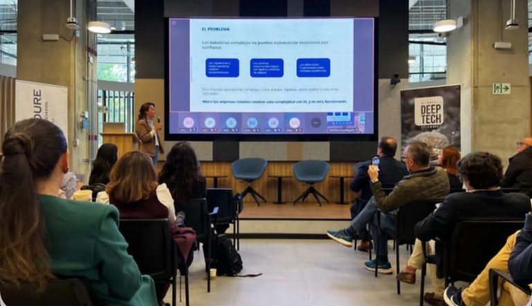 Una mujer presenta una diapositiva titulada “El problema” en el lanzamiento del reporte Sciencepreneurs: DeepTech Colombia 2025 en el Centro de Innovación Campus Bogotá. La pantalla grande muestra una presentación con cuadros azules y texto en español, y a la derecha hay un cartel que dice “Deep Tech”. El evento ocurre en un auditorio moderno con ventanales grandes y público tomando fotos o escuchando la charla.
